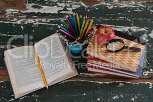 Stack of books with apple, magnifying glass and pen holder