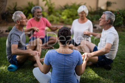 Trainer holding hands and meditating with senior men and women