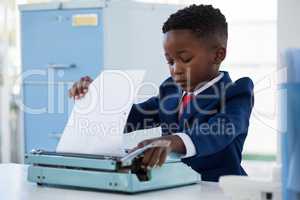 Boy imitating as businessman adjusting paper on typewriter