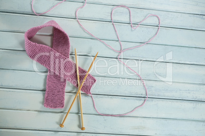 High angle view of pink woolen Breast Cancer Awareness ribbon by crochet needles with heart shape