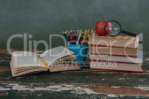 Stack of books with apple, magnifying glass and pen holder