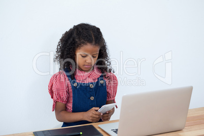Businesswoman using phone while sitting by laptop