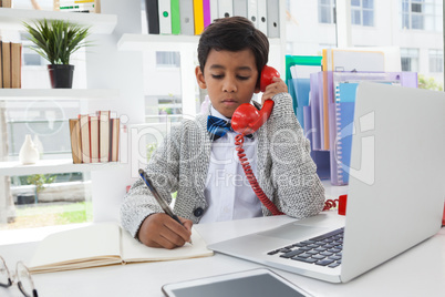 Businessman writing on book while talking on landline phone