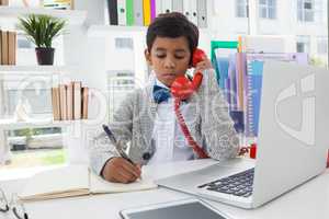 Businessman writing on book while talking on landline phone