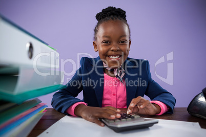 Portrait of smiling businesswoman using calculator at desk