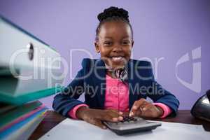Portrait of smiling businesswoman using calculator at desk