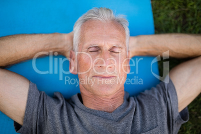 Senior man resting with closed eyes on mat at park