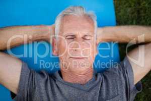 Senior man resting with closed eyes on mat at park