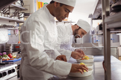 Two chefs garnishing food in commercial kitchen