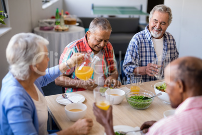 Senior female serving drink to male friends