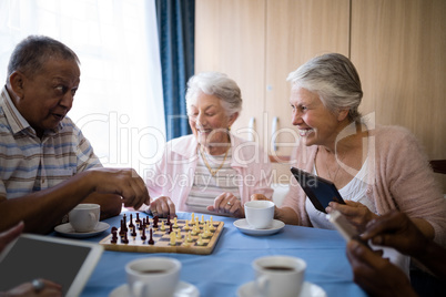 Happy senior friends playing chess while having coffee