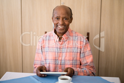 Portrait of smiling senior man sitting with digital tablet at table