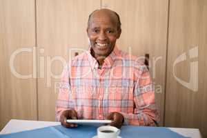 Portrait of smiling senior man sitting with digital tablet at table