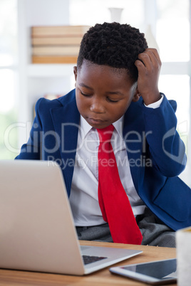 Confused businessman with hand in hair using laptop