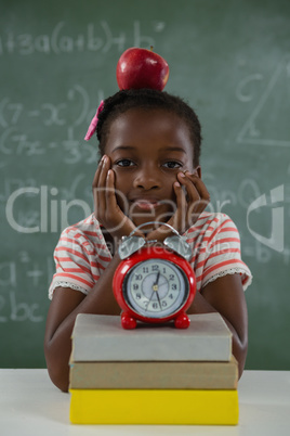 Schoolgirl sitting with red apple on her head against chalkboard