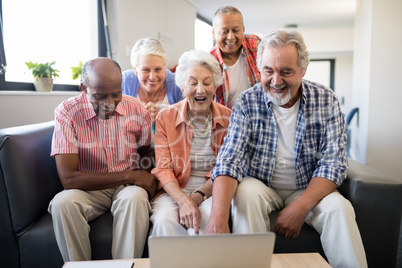 Cheerful senior friends looking at laptop on table