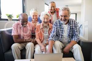 Cheerful senior friends looking at laptop on table