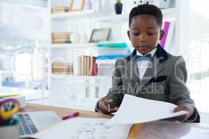 Businessman turning pages on document by laptop at desk