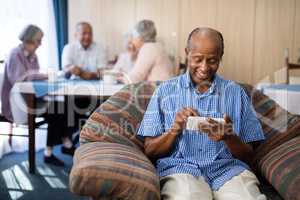 Happy senior man using phone while sitting on couch