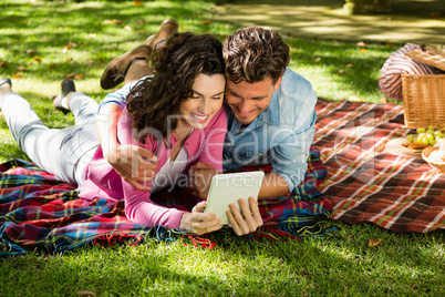 Couple lying on picnic blanket and using digital tablet