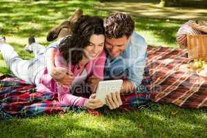 Couple lying on picnic blanket and using digital tablet
