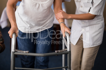 Midsection of female doctor assisting senior woman walking with walker