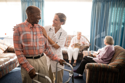 Smiling senior man with walker looking at female doctor against window