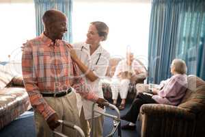Smiling senior man with walker looking at female doctor against window