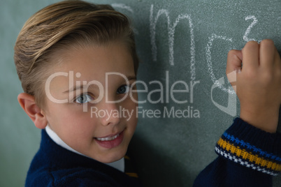 Schoolboy writing maths formula on chalkboard