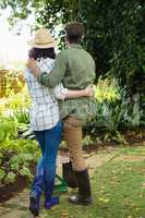 Rear view of couple standing with gardening rake and shovel in garden
