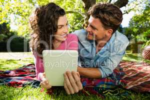 Couple lying on picnic blanket and using digital tablet