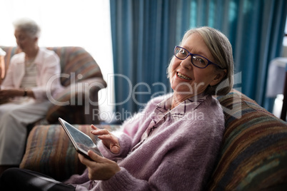 Portrait of smiling senior woman sitting with digital tablet on armchair