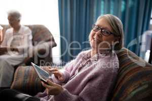 Portrait of smiling senior woman sitting with digital tablet on armchair