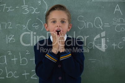 Surprised schoolboy standing against chalkboard