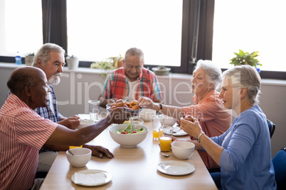 Senior man giving food to friends sitting at table