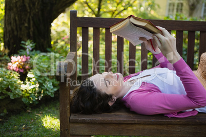 Woman reading a book while lying on a bench