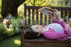 Woman reading a book while lying on a bench