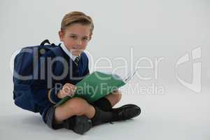 Schoolboy reading book while sitting on white background