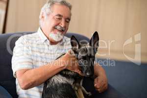 Happy senior man stroking puppy while sitting on armchair