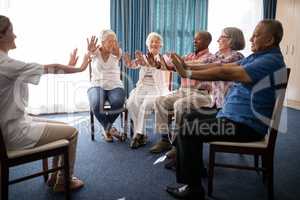 Female doctor and seniors exercising on chairs