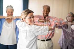 Rear view of smiling female doctor exercising with senior people