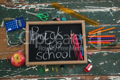 Back to school text written on chalkboard with various stationery and apple