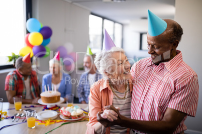 Happy senior couple wearing party hats with friends