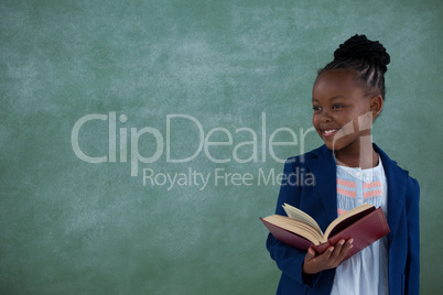 Businesswoman reading book while standing against blackboard