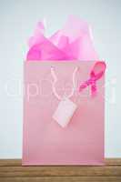 Close-up of pink Breast Cancer Awareness ribbon on shopping bag over wooden table
