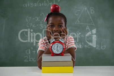 Schoolgirl sitting with red apple on her head against chalkboard