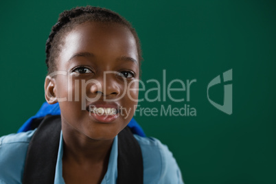 School girl with backpack standing against chalk board