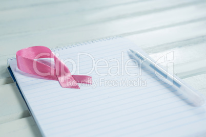 Close-up of pink Breast Cancer Awareness ribbon and spiral notepad with pen