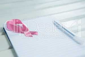 Close-up of pink Breast Cancer Awareness ribbon and spiral notepad with pen