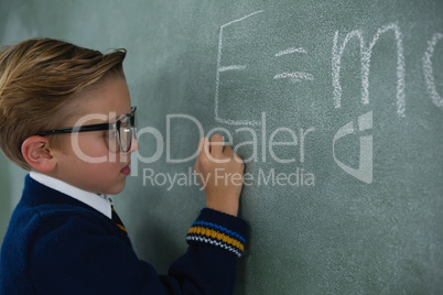 Schoolboy writing maths formula on chalkboard